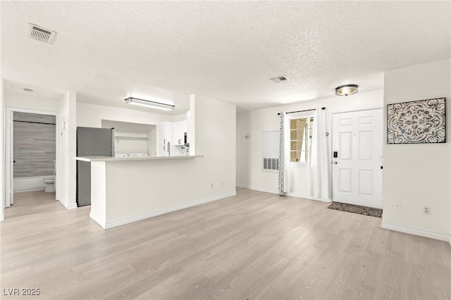 unfurnished living room with a textured ceiling, light wood finished floors, and baseboards