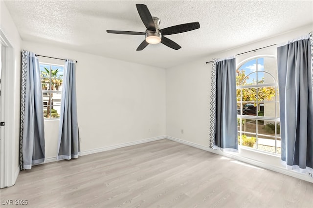 unfurnished room with a textured ceiling, plenty of natural light, wood finished floors, a ceiling fan, and baseboards