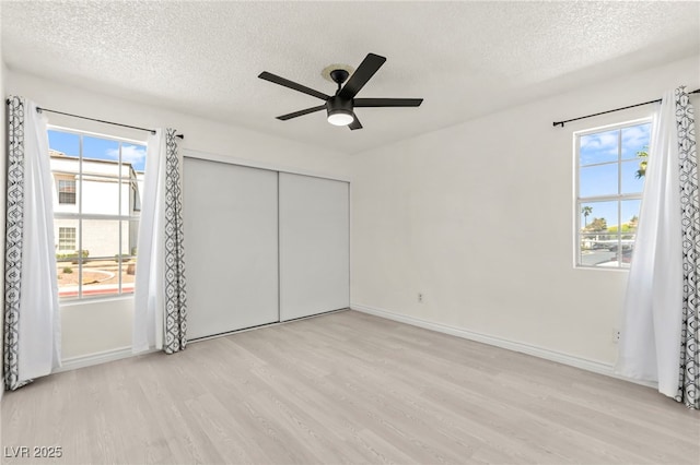 unfurnished bedroom with light wood-style flooring, a textured ceiling, multiple windows, and baseboards