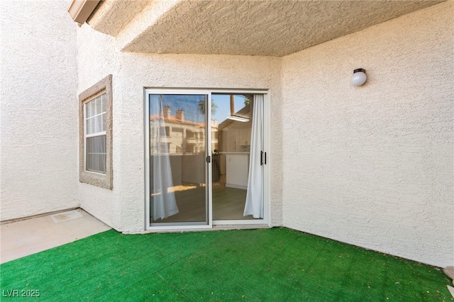 doorway to property featuring stucco siding and a lawn