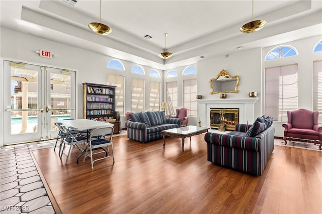 living room with a raised ceiling, wood finished floors, french doors, and a glass covered fireplace