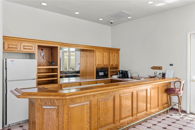 kitchen with freestanding refrigerator, black microwave, a peninsula, light floors, and recessed lighting