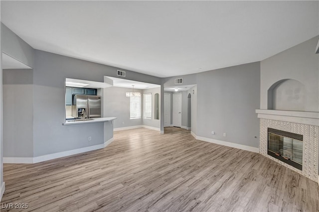1501 Oscar Ct Unit 101, Las Vegas, NV 89146 - unfurnished living room featuring a tiled fireplace, light wood finished floors, a chandelier, and baseboards