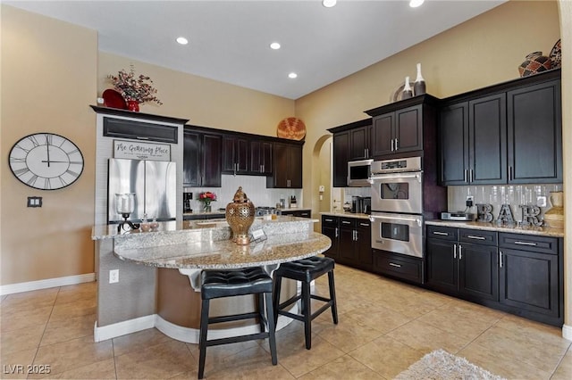 7719 Villa Montara St, Las Vegas, NV 89123 - kitchen featuring stainless steel appliances, light tile patterned flooring, tasteful backsplash, a center island with sink, and light stone countertops