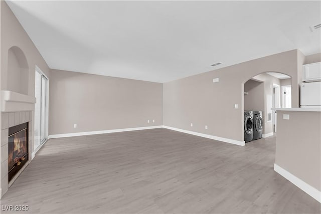 4324 W Lake Mead Blvd Unit 202, Las Vegas, NV 89108 - unfurnished living room featuring separate washer and dryer, a tiled fireplace, light wood-type flooring, baseboards, and arched walkways