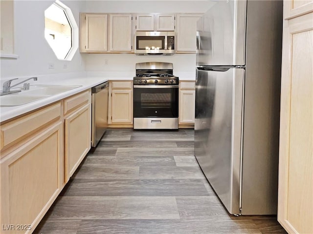 kitchen with stainless steel appliances, a sink, light brown cabinetry, and wood finished floors