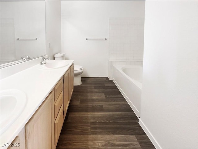 full bathroom featuring wood finished floors, baseboards, toilet, a tub to relax in, and double vanity