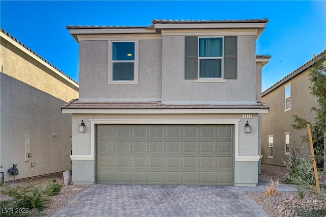traditional-style home with an attached garage, stucco siding, decorative driveway, and a tiled roof