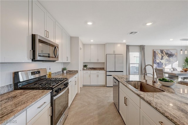 kitchen featuring appliances with stainless steel finishes, a sink, white cabinets, light tile patterned floors, and light stone countertops