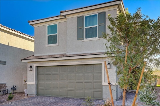 traditional-style house featuring an attached garage, stucco siding, and decorative driveway
