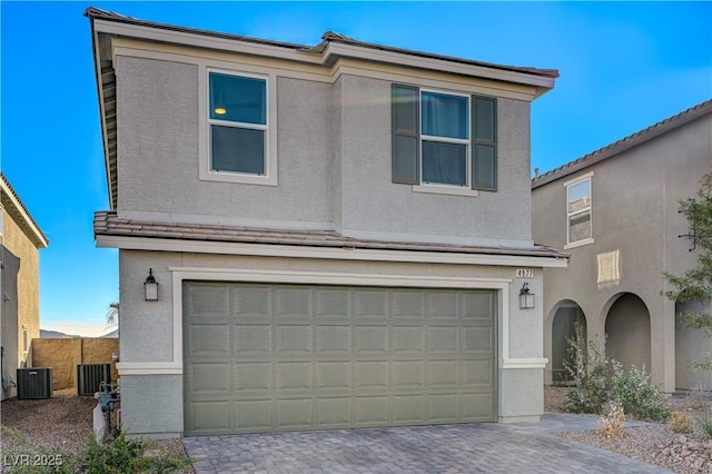 view of front of house featuring a garage, central AC, stucco siding, and decorative driveway