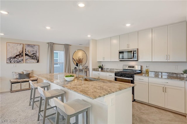kitchen featuring appliances with stainless steel finishes, a sink, light stone counters, an island with sink, and a kitchen breakfast bar