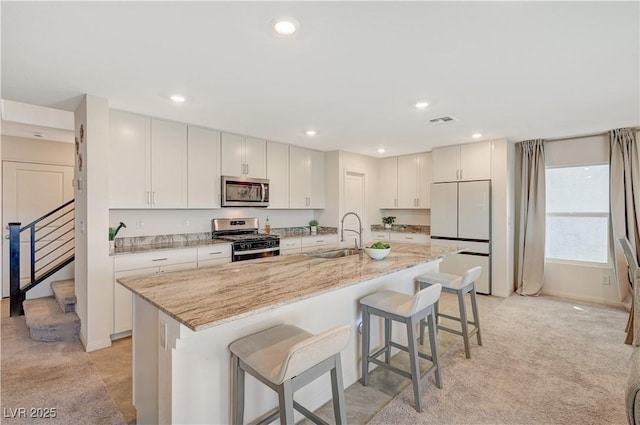 kitchen featuring stainless steel appliances, a sink, a breakfast bar, a center island with sink, and light stone countertops
