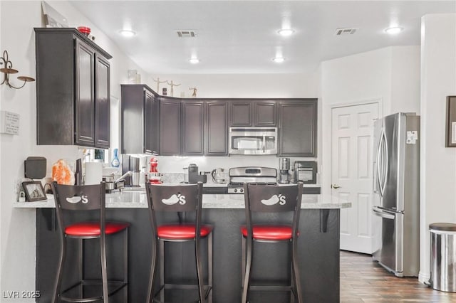 3632 Julia Waldene Ct, Las Vegas, NV 89129 - kitchen with appliances with stainless steel finishes, a peninsula, dark wood-style floors, dark brown cabinets, and a kitchen breakfast bar