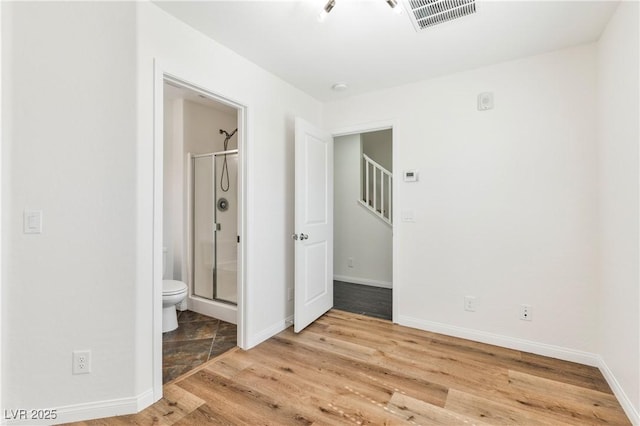 unfurnished bedroom featuring wood finished floors, baseboards, and ensuite bathroom
