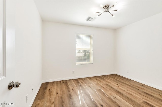 spare room featuring a chandelier, light wood-style flooring, and baseboards