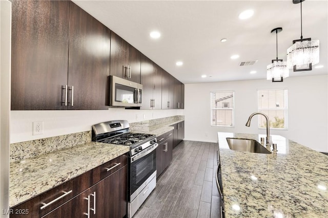 kitchen with appliances with stainless steel finishes, a sink, dark wood-type flooring, recessed lighting, and light stone counters