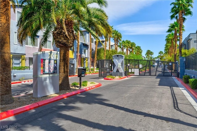 view of asphalt street with a gate, a gated entry, and curbs