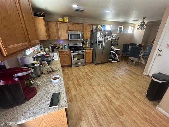 kitchen with stainless steel appliances, brown cabinets, light countertops, light wood finished floors, and recessed lighting