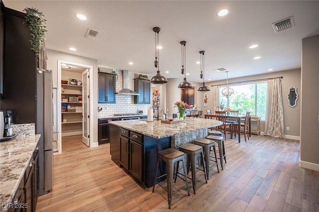 3698 Regatta Landing Dr, Las Vegas, NV 89141 - kitchen with wall chimney exhaust hood, a breakfast bar, a center island with sink, tasteful backsplash, and light wood-style flooring