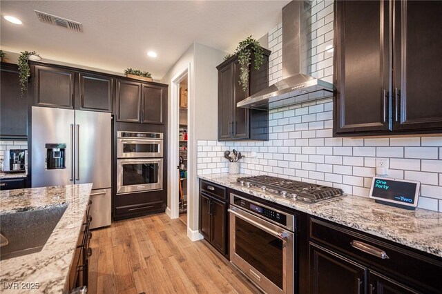 3698 Regatta Landing Dr, Las Vegas, NV 89141 - kitchen with wall chimney exhaust hood, appliances with stainless steel finishes, light wood finished floors, light stone countertops, and recessed lighting
