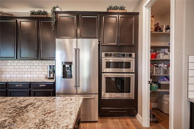 3698 Regatta Landing Dr, Las Vegas, NV 89141 - kitchen with stainless steel appliances, light wood finished floors, light stone counters, dark brown cabinets, and backsplash