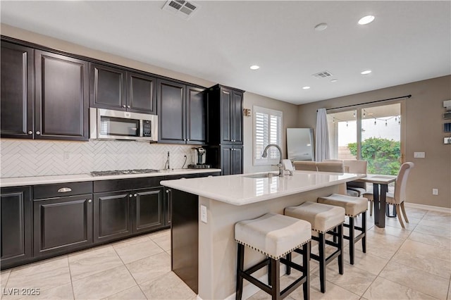 kitchen with appliances with stainless steel finishes, a sink, light countertops, a breakfast bar area, and decorative backsplash