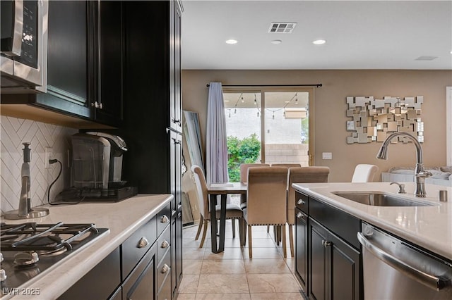 kitchen featuring stainless steel appliances, a sink, dark cabinetry, light countertops, and backsplash