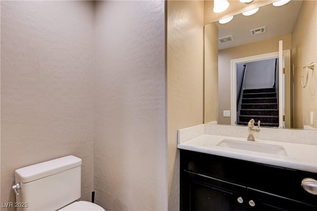 half bath with toilet, vanity, and a textured wall