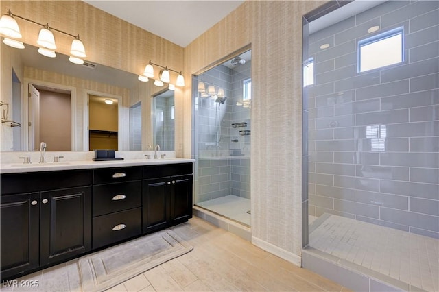 bathroom featuring walk in shower, wallpapered walls, double vanity, and wood finished floors