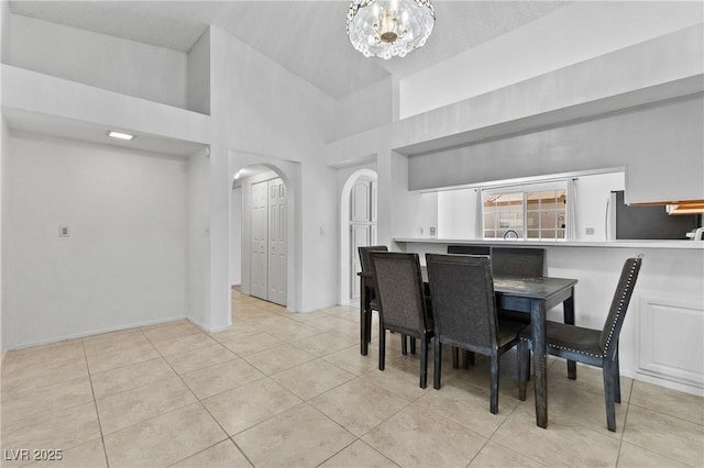 dining area featuring arched walkways, tile patterned flooring, a chandelier, high vaulted ceiling, and baseboards
