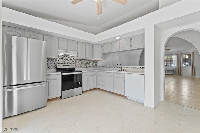 kitchen featuring stainless steel appliances, a sink, under cabinet range hood, light countertops, and arched walkways