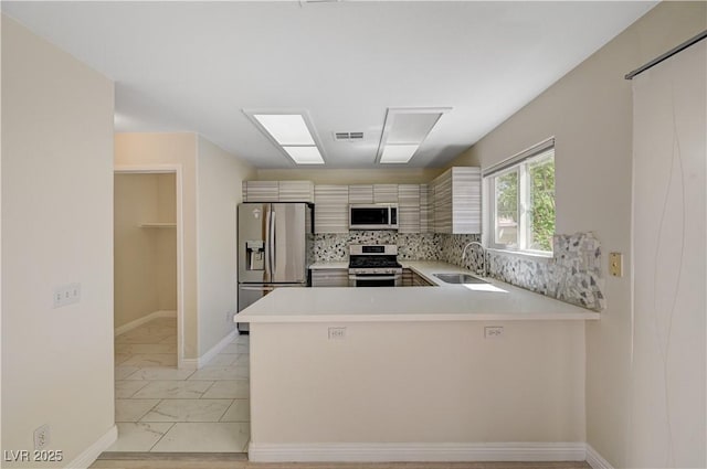 kitchen featuring appliances with stainless steel finishes, a sink, light countertops, light marble finish flooring, and a peninsula