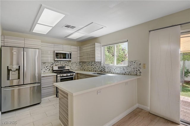 kitchen with stainless steel appliances, light countertops, tasteful backsplash, a sink, and a peninsula