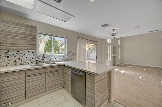 kitchen featuring a sink, dishwasher, a peninsula, open floor plan, and light countertops