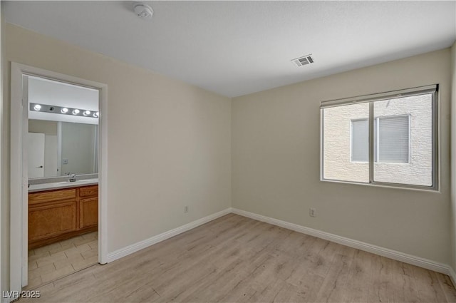 unfurnished bedroom with light wood-style floors, baseboards, and ensuite bath