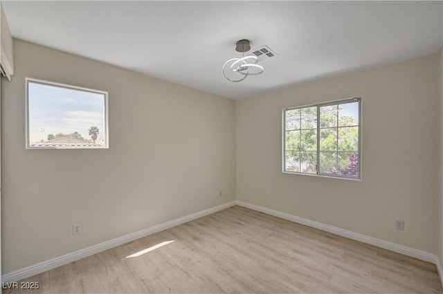 spare room with light wood-type flooring, baseboards, and a chandelier