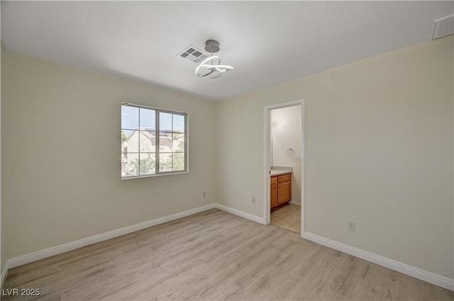 unfurnished bedroom featuring light wood-style floors, baseboards, and ensuite bathroom