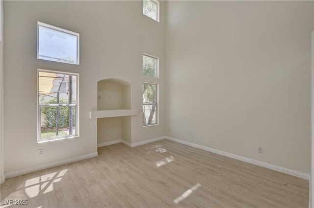 unfurnished room featuring healthy amount of natural light, light wood-style floors, baseboards, and a towering ceiling