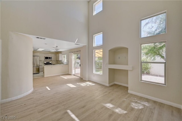 unfurnished living room with a high ceiling, baseboards, light wood finished floors, and ceiling fan