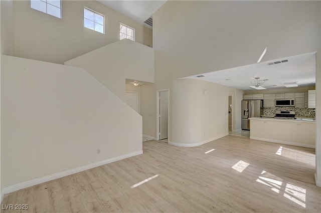 unfurnished living room featuring light wood-type flooring, baseboards, a high ceiling, ceiling fan, and a sink