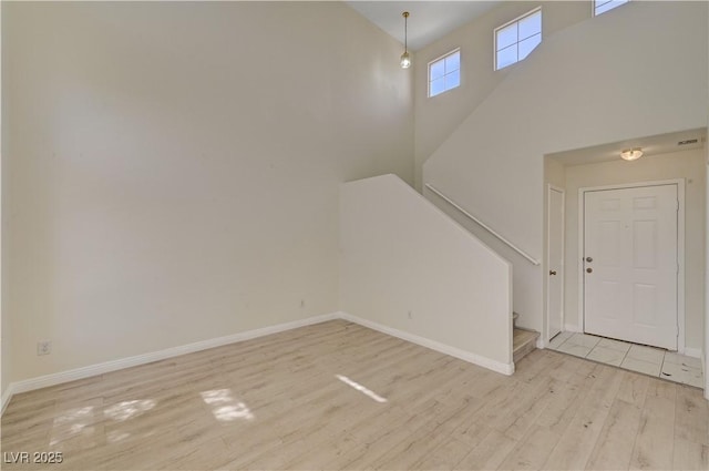 unfurnished living room with light wood finished floors, baseboards, stairway, and a high ceiling