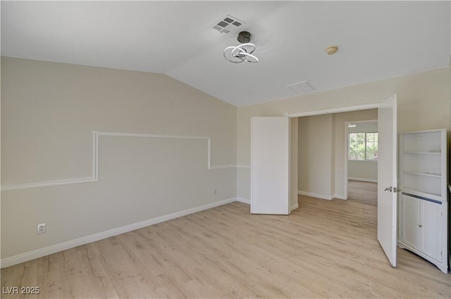 empty room featuring lofted ceiling, light wood-style floors, and baseboards