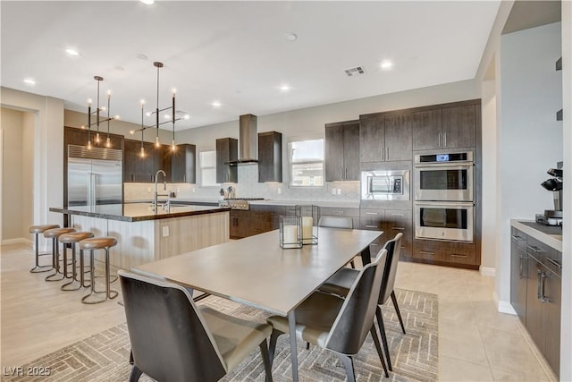 11280 Granite Ridge Dr Unit 1035, Las Vegas, NV 89135 - kitchen featuring built in appliances, a large island with sink, a sink, wall chimney range hood, and dark brown cabinetry