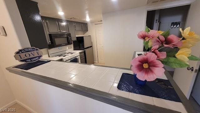 1830 N Pecos Rd Unit 155, Las Vegas, NV 89115 - kitchen featuring black microwave, white gas stove, freestanding refrigerator, tile counters, and recessed lighting