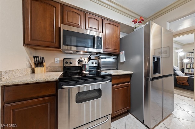 kitchen featuring stainless steel appliances, ornamental molding, light tile patterned flooring, light stone countertops, and brown cabinets
