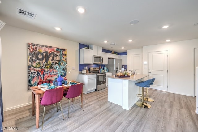 kitchen featuring appliances with stainless steel finishes, light wood-style flooring, an island with sink, recessed lighting, and a kitchen bar