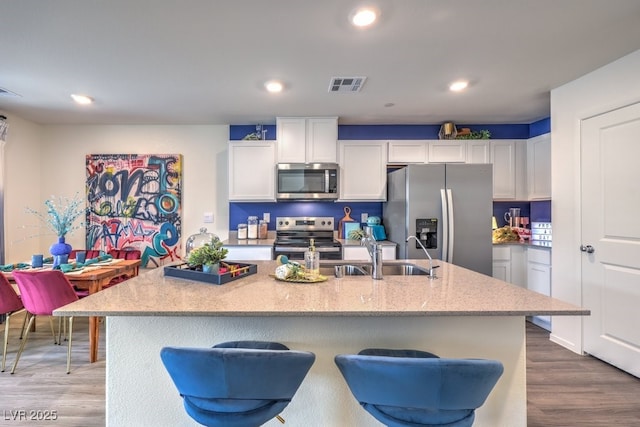kitchen featuring stainless steel appliances, a sink, white cabinetry, dark wood-style flooring, and light stone countertops