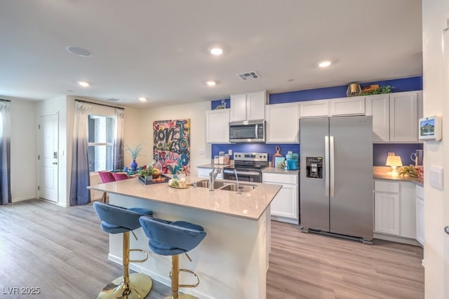 kitchen with stainless steel appliances, a sink, light wood finished floors, white cabinets, and recessed lighting