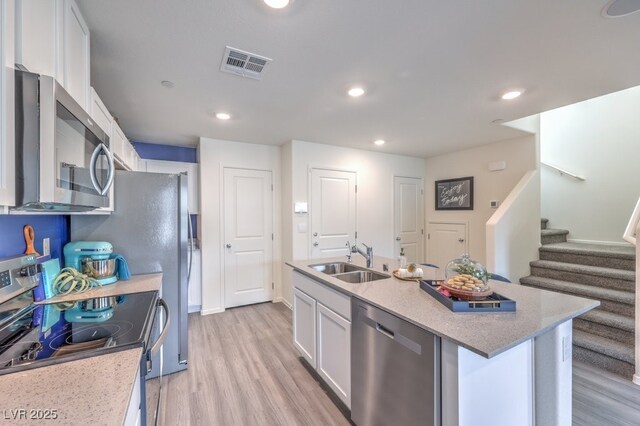 kitchen with a sink, stainless steel appliances, white cabinetry, light wood-type flooring, and a kitchen island with sink